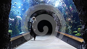 Young female walking in huge aquarium tunnel, enjoying a underwater sea inhabitants. world traveling concept. sealife