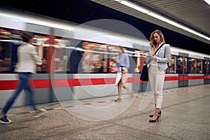 Young female watching at her cell phone in a subway with people and train goes by. Time concept