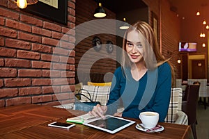 Young female is watching video on digital tablet during rest in modern coffee shop