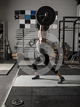 Young female weight lifter struggles with putting a heavy barbell over her head