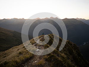 Young female woman hiking along remote alpine mountain ridge path, Brewster Hut Haast Valley, Southern Alps New Zealand