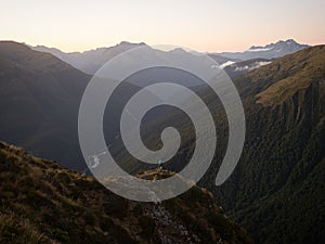 Young female woman hiking along remote alpine mountain ridge path, Brewster Hut Haast Valley, Southern Alps New Zealand