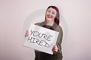 Young female woman holding a message board with You`re Hired written in black ink