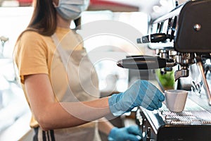 Young female working inside bar restaurant while making coffee wearing gloves and face mask for coronavirus spread prevention -