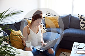 Young female working on tablet computer sat on sofa