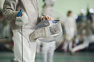 Young fencer holding foil and protective mask in his hand on the fencing tournament