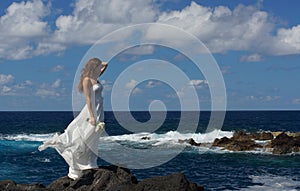 Young fiancee in wedding dress standing on rocks on sea shore, Sao Miguel island, Azores