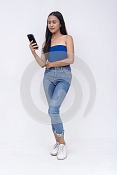 A young Filipino woman in a blue tube top and jeans browsing on her cellphone. Full body photo isolated on a white background