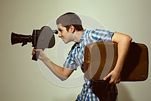 Young filmmaker with old movie camera and a suitcase in his