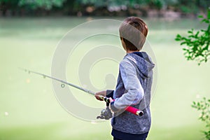 Young fisher. Boy fishing at river bank, summer outdoor. Young boy sitting at river bank with rod and fishing. Summer leisure