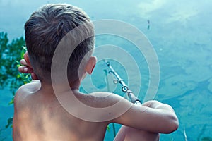 Young fisherman catches fish in river on hot summer day. boy has cast bait and is waiting for bite, sitting with his back to