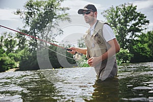 Young fisherman fishing on lake or river. Active guy in professional rob or clothes stand in water and trying to catch