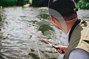 Young fisherman fishing on lake or river. Back view of guy holding fishing rod in hand and looking at water. Lake fish