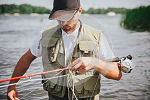 Young fisherman fishing on lake or river. Busy serious concentrated guy holding rod and fishing line in hands. Preparing