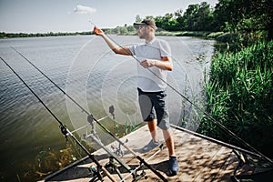 Young fisherman fishing on lake or river. Guy has three rods fishing and trying to find fish in water. Man working on