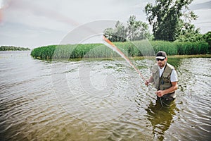 Young fisherman fishing on lake or river. Picture of guy in robe holding fishing line straight to camera. Man stand in