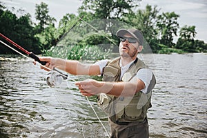 Young fisherman fishing on lake or river. Serious concentrated guy holding rod in hands and using it for fishing