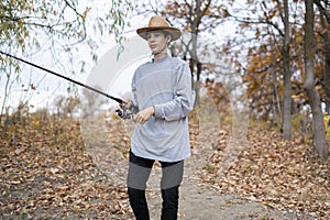 Young fisherman in hat fishing with rod in forest lake f