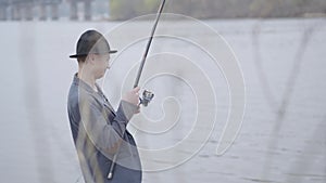 Young fisherman in a jacket and a cap with a brim in the early morning catch scomber fish with spinning in river near