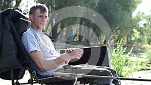 Young fisherman sitting on chair by river nearly fishing rod waiting for bite