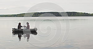 Young fishermen on an inflatable boat on the lake are fishing. Cinematic shot.