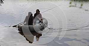 Young fishermen on an inflatable boat on the lake are fishing. Cinematic shot.