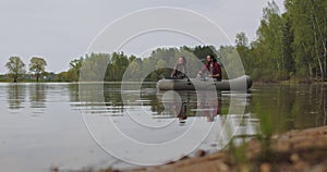 Young fishermen on an inflatable boat on the lake are fishing. Cinematic shot.