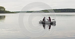 Young fishermen on an inflatable boat on the lake are fishing. Cinematic shot.