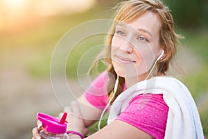 Young Fit Adult Woman Outdoors With Towel and Water Bottle in Workout Clothes Listening To Music with Earphones.