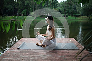 Young fit asian woman doing yoga by the lake in the morning park