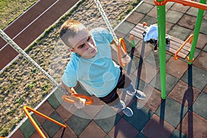 Young fit athlete working out at outdoor gym making dipping pull ups exercise using dip rings
