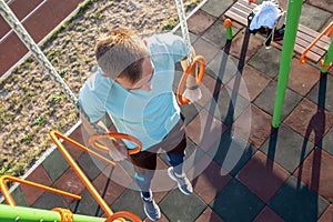 Young fit athlete working out at outdoor gym making dipping pull ups exercise using dip rings