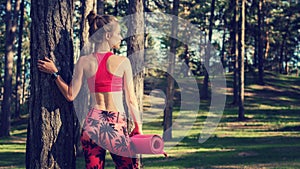 Young fit athletic woman in a forest wearing smart watch and holding yoga mat. Mind and body concept with copy space.