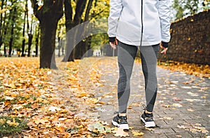 Young fit athletic woman wears modern running clothes standing on the footway before jogging in the autumnal city park. Active photo