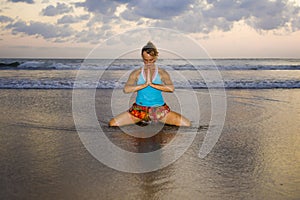 Young fit and attractive sport woman in beach sunset yoga practice workout sitting on wet sun in front of the sea in meditation an