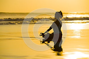 Young fit and attractive sport woman in beach sunset yoga practice workout sitting on wet sun in front of the sea in meditation an