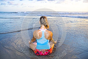 Young fit and attractive sport woman in beach sunset yoga practice workout sitting on wet sun in front of the sea in meditation an
