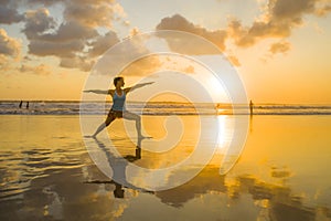 Young fit and attractive sport woman in beach sunset yoga practice workout on wet sun in front of the sea in meditation and relaxa