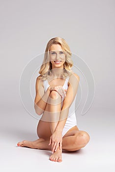 Young, fit and beautiful blond woman in white swimsuit posing over grey. Healthcare, diet, sport and fitness concept.