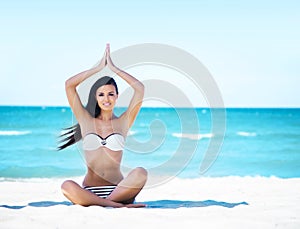 Young, fit and beautiful girl meditating on the beach