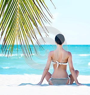 Young, fit and beautiful girl meditating on a summer beach