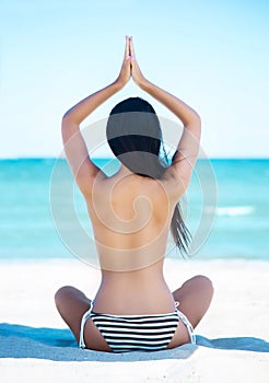Young, fit and beautiful girl meditating on a summer beach