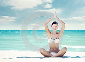 Young, fit and beautiful girl meditating on a summer beach