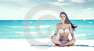 Young, fit and beautiful girl meditating on a summer beach