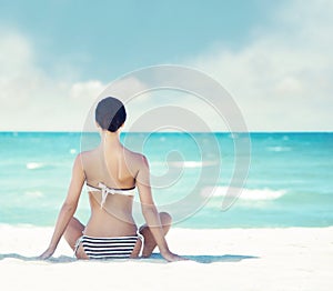 Young, fit and beautiful girl meditating on a summer beach