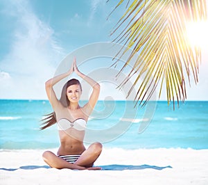 Young, fit and beautiful girl meditating on a summer beach