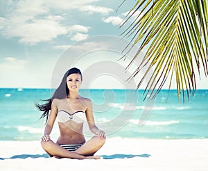 Young, fit and beautiful girl meditating on a summer beach