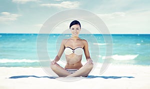 Young, fit and beautiful girl meditating on a summer beach