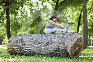 Young fit beautiful girl resting and stretching on a tree log