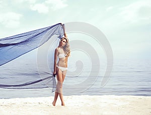 Young, fit, sporty and beautiful girl with a blowing silk posing on a beach.